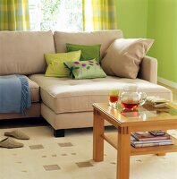 Beige Sofa mit Kissen in Beige und Grün, davor ein Holz - Besitelltisch