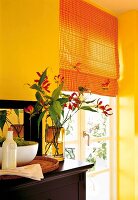 Am Fenster Faltrollos orange kariert rote Blumen im Glas, Stück Wand gelb