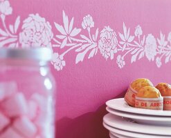 Schablonenmalerei auf der Wand weiße Bordüre auf rosa Tapete