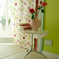 Flower vase with roses and books on folding table against green wall