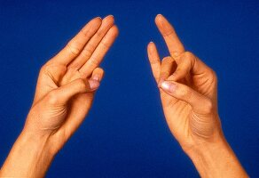 Close- up of woman's hand performing acupressure mudra against blue background