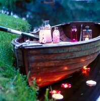 Various lanterns in boat and tea light floating on water