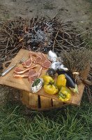Brett mit Lammkoteletts, Gemüse und, Kartoffeln neben der Feuerstelle