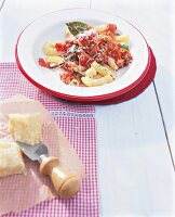 Tortiglioni alla Bolognese next to parmesan cheese on checked napkin