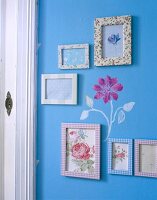 Bunte Bilderrahmen hängen an blauer Wand mit aufgemalter Blume