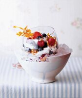 Glass of fresh berries, yogurt and almond in bowl of ice cubes