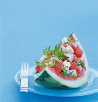 Salad with feta arranged on melon with folk kept on blue plate