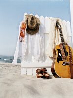 Kleidung hängt am Holzzaun am Strand, Schuhe, Gitarre