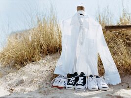 weißes Hemd am Kleiderbügel am Holzpfahl, davor Turnschuhe, Strand