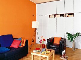 weiße Schrankwand, Wand orange, Ledersessel, Beistelltisch aus Holz
