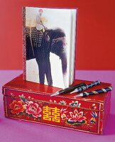 Travel diary, pen and Chinese box on pink background