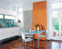 Küche in Weiß: Metalltisch mit Glas- Platte, Stühle, Teil der Wand gelb