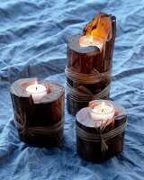 Drei Kerzen brennen in ausgehöhlten Holzscheiten