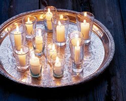 Kerzen in  Wassergläsern stehen auf einem Silbertablett verteilt
