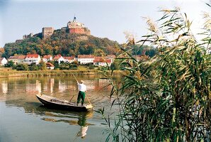Man standing in boat on river in front of castle and houses