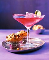 A red cocktail in a glass next to two muffins