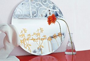Spiegel mit zarten, goldenen Blütenranken, daneben Vase mit Blume