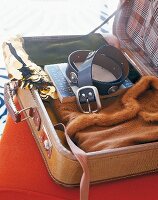 Gepackter Koffer mit Klamotten, Buch und Ledergürtel mit Nieten.