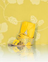 Gelbe Sandale, Gürtel und Handtasche vor geblümten Hintergrund.