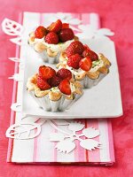 Three mascarpone and strawberry tartlets in silver cases on a plate
