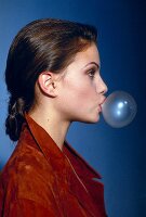 Side view of woman with brown hair blowing bubble with chewing gum