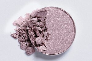 Close-up of broken mauve eye shadow on white background