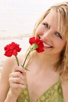 Woman wearing green halterneck dress holding red flower on beach, laughing