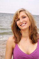 Portrait of beautiful woman wearing purple top standing on beach, smiling