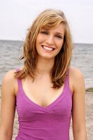 Portrait of beautiful woman wearing purple top standing on beach, smiling