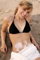 Portrait of pretty woman wearing lingerie lying on sand with salt crystals on belly