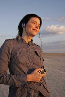 Pretty woman wearing brown shirt and jeans listening music, looking away and smiling