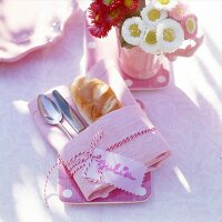 Cutlery and bread rolls wrapped in pink napkin with name tag