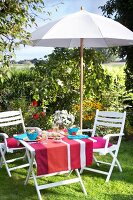 Table with colourful striped tablecloth laid under an umbrella in garden