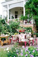 Metal table with chairs, table cloth, flower vase and food trolley in garden terrace