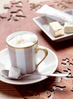 Eine Tasse Milchkaffee mit Schoko- riegeln und Zuckerstück auf Löffel.x