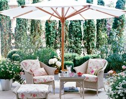 Wicker chair with floral patterned cushions under white parasol in garden