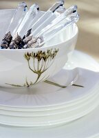 Close-up of white bowl with cutlery and motifs on stack of plates