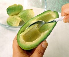 Close-up of flesh being scooped from halved avocado with a spoon