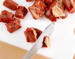 Close-up of meat cut in dice with knife on white chopping board