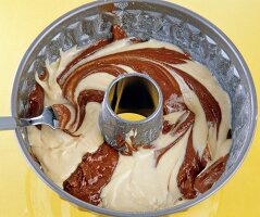 Gugelhupf with light and dark batter being stirred in baking bowl on yellow background
