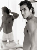 Portrait of shirtless man in white underwear standing in front of mirror