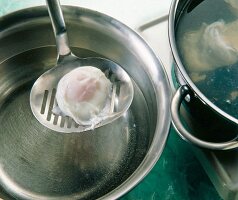 Close-up of poached eggs being removed from a pan with skimmer