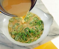 Close-up of eggs and cream being poured over spring onions on plate