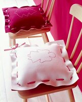 Red and pink embroidered felt cushions with angel and Christmas tree motif on wooden chair