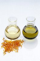 Two flasks containing oil with dried flower petals against white background