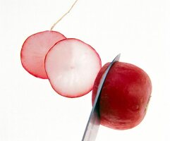 Slices of radishes with a knife on white background