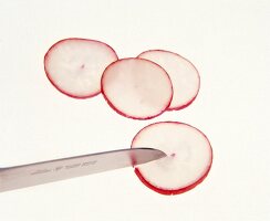 Slices of radishes being cut in half with knife on white background