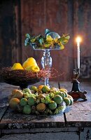 Lit candles, chaenomeles on glass stand and several fruits on table