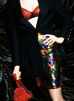 Mid section of woman sequined bra, blazer, skirt and holding red handbag with hand on hip