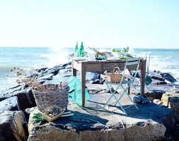 Table laid on rock with food next to basket against sea